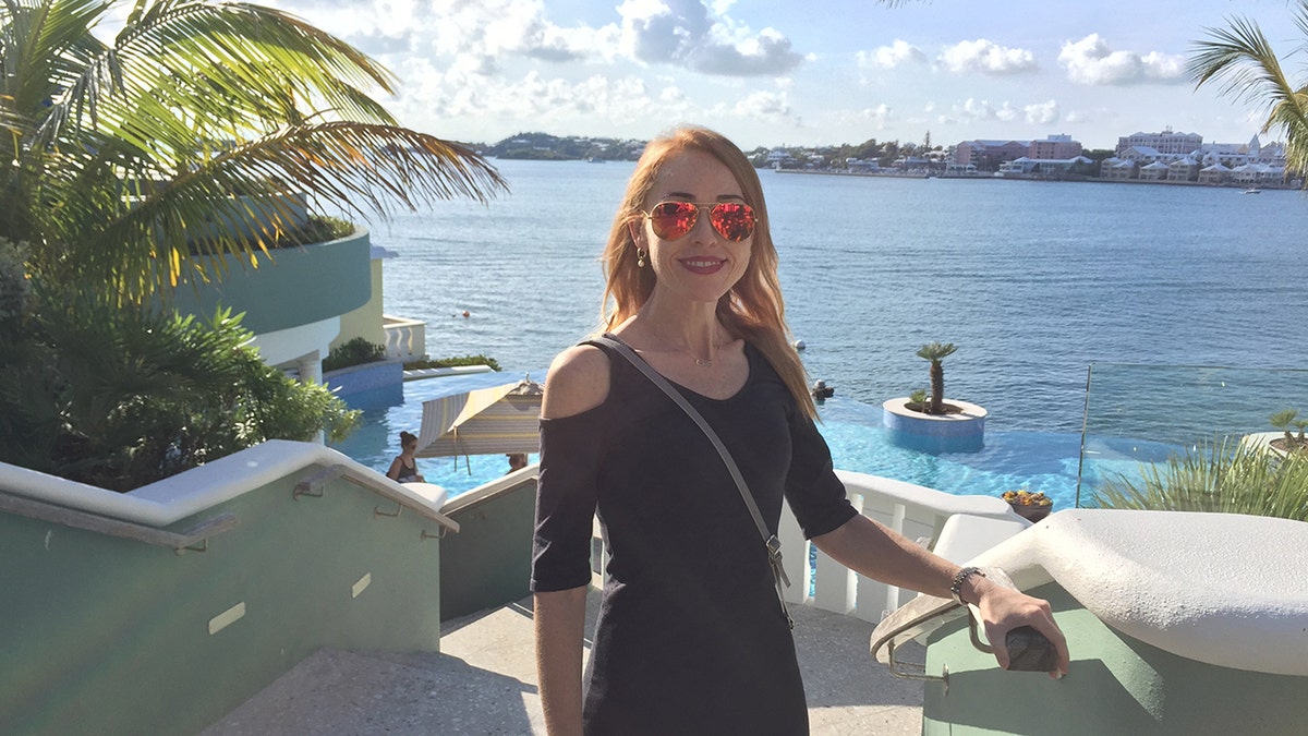 Terrilyn Griffith standing in front of an ocean view. The blonde woman has sunglasses on and she is smiling. Pre-injury.