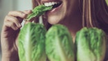 Close-up shot of a woman chewing on some romaine lettuce. We only see her mouth. She is smiling.