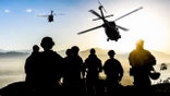 Silhouettes of soldiers during Military Mission at dusk, choppers fly overhead as sunlight peaks through mountains in the distance
