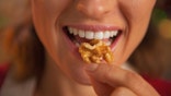Woman eating walnut, only her lips are shown as she smiles and holds the walnut up to her mouth.