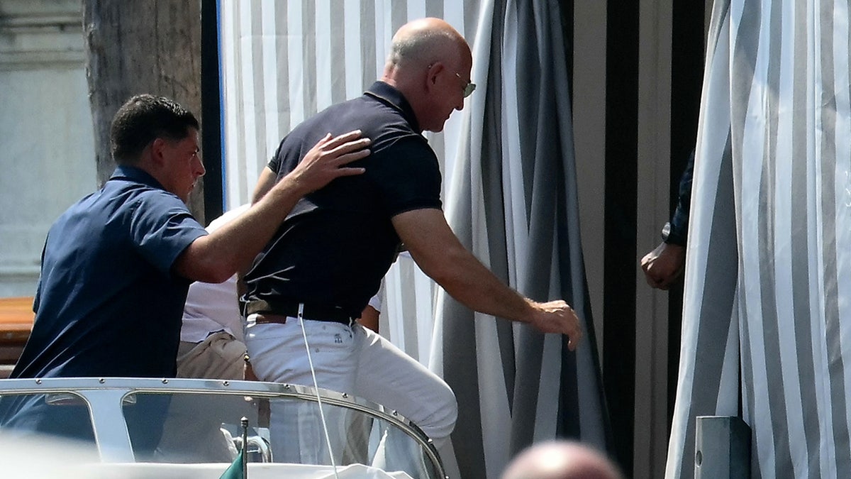 Jeff Bezos in white pants and a black polo stepping off a boat in Venice