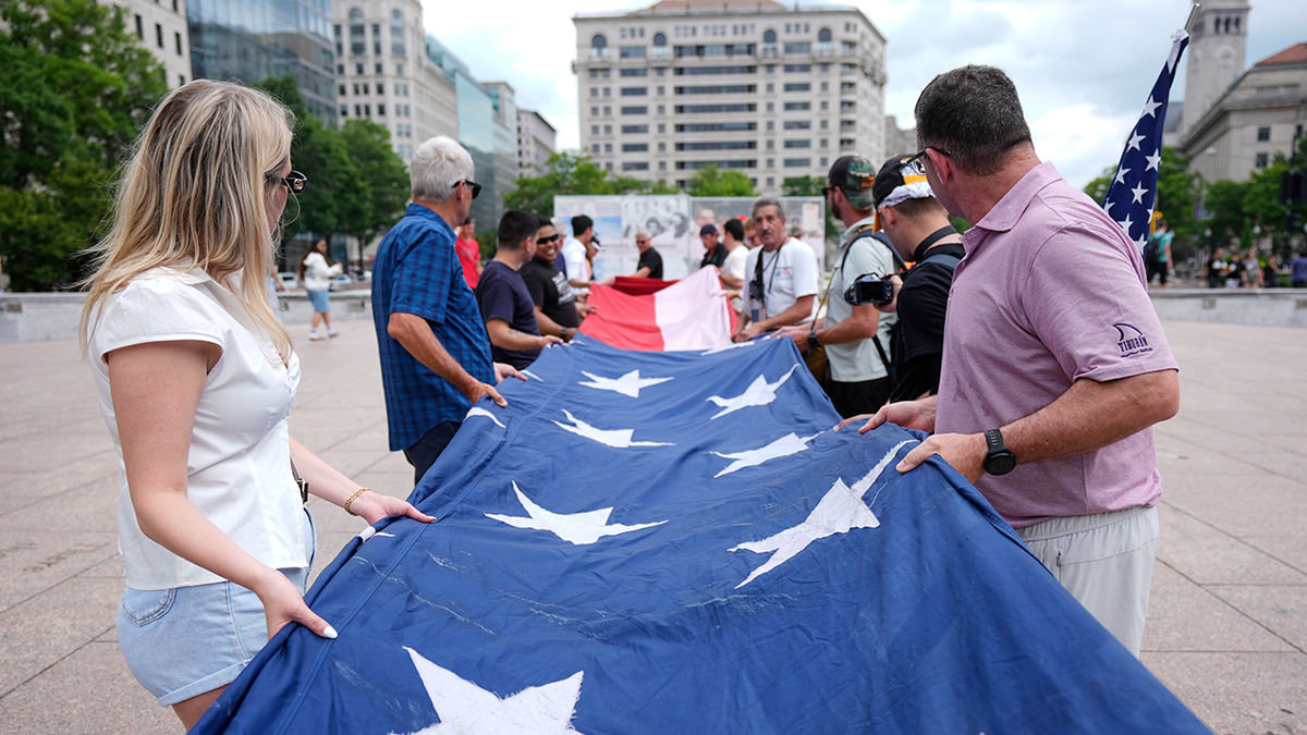 As pessoas dobraram uma grande bandeira americana no Freedom Plaza antes de uma marcha em memória do aniversário de dois e -Half -Half -Haly em Washington no sábado, 7 de junho de 2021.