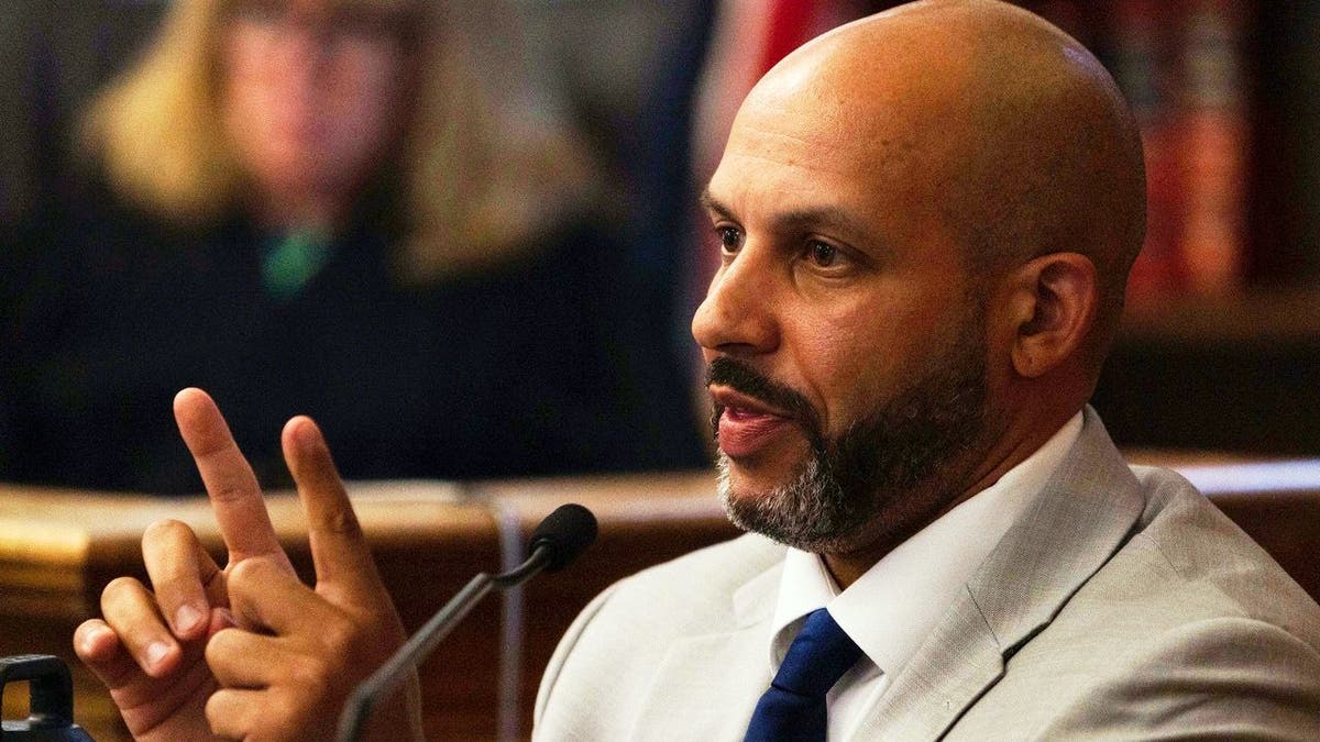 Dighton Police Sgt. Nicholas Barros gestures while wearing a gray suit on the witness stand