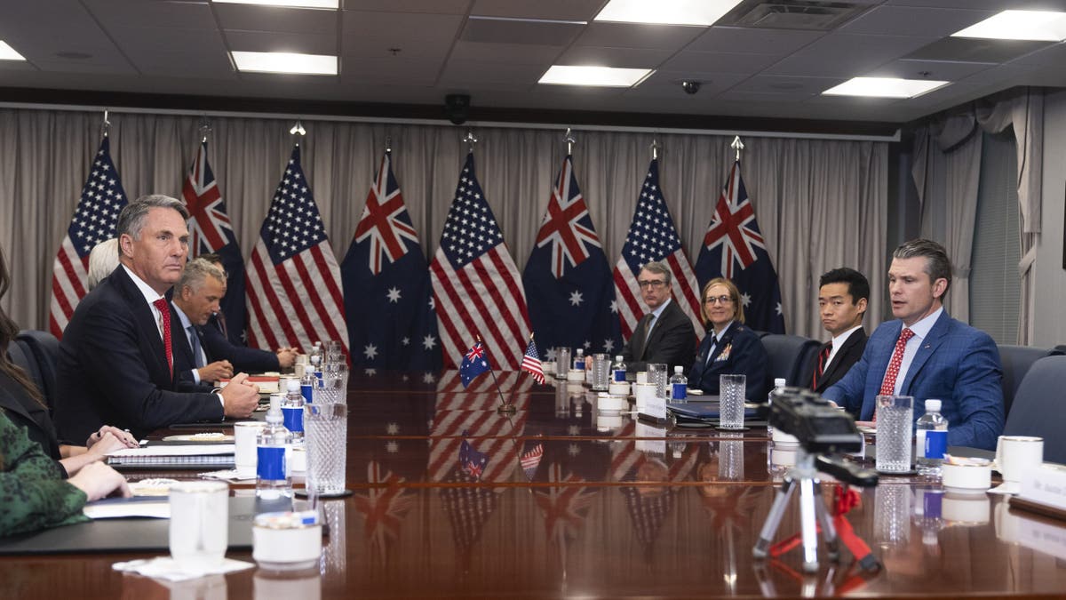 U.S. and Australian defense officials meet at the Pentagon with national flags displayed behind them, discussing military cooperation.