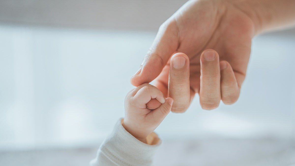 Close up of a small hand of a baby child holding a mother's hand