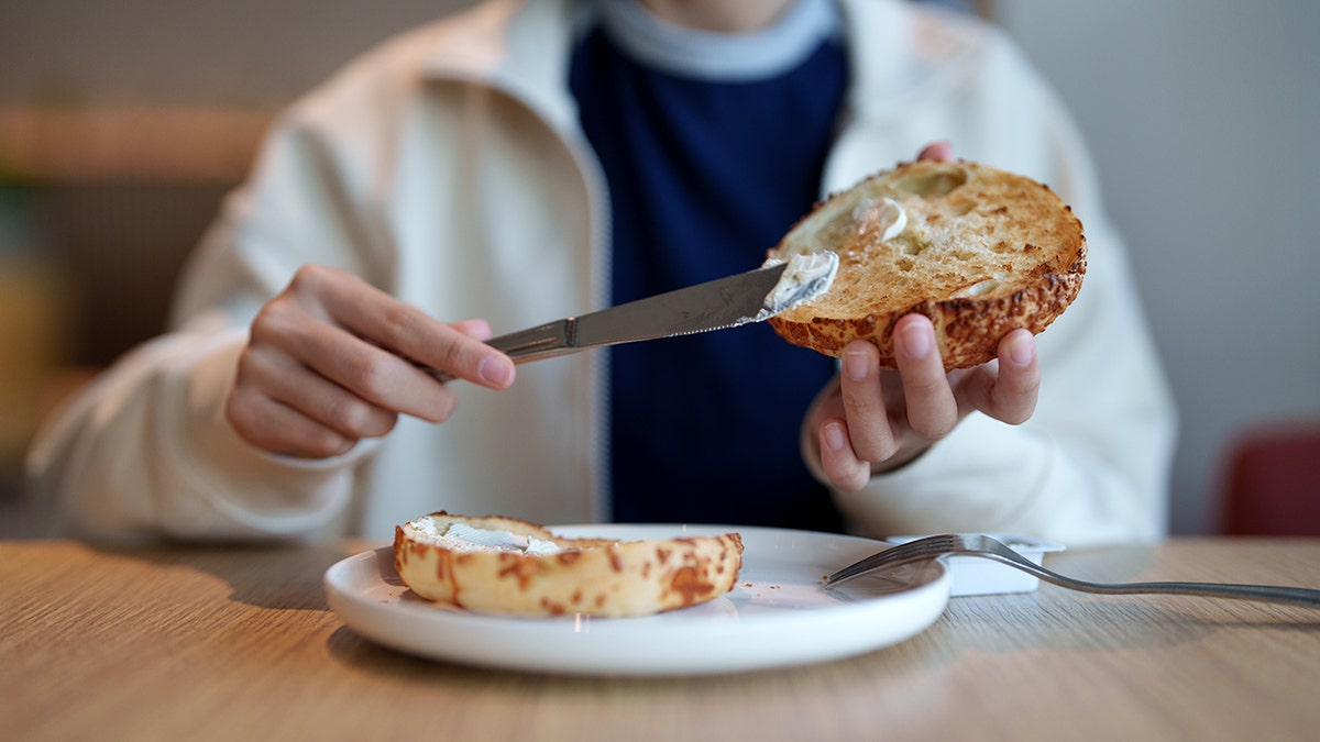 Foreground of the person who extends cream cheese on a slice of Bagel for breakfast.
