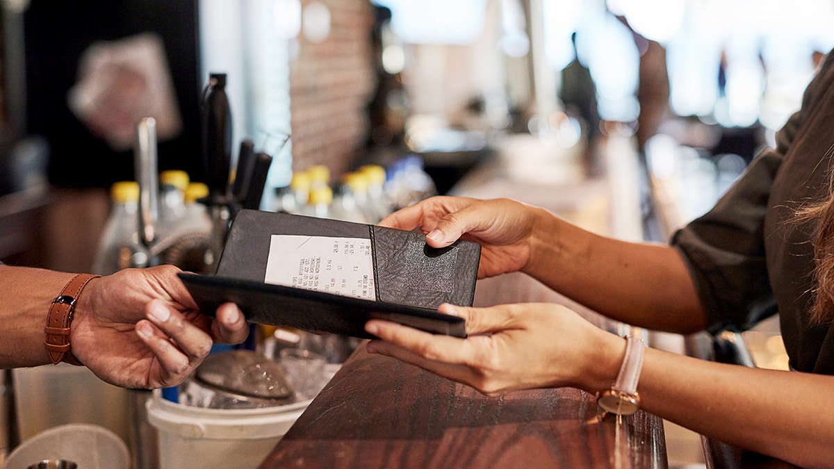 A bartender's hand receives a check from a woman at a bar.