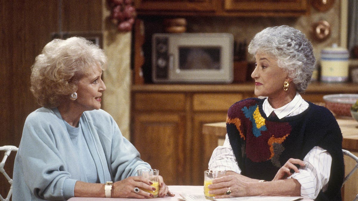 betty white and bea arthur looking at each other while seated at a table