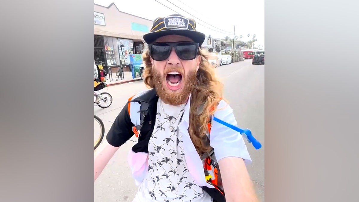 US comedian Sebastian Fowler pictured on his bike while BMXing across America, wearing sunglasses and a 'thrill seekers' hat
