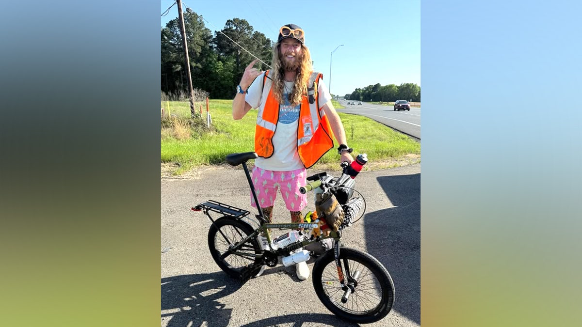 US comedian Sebastian 'Seabass' Fowler posing behind his BMX beside a highway, smiling at the camera