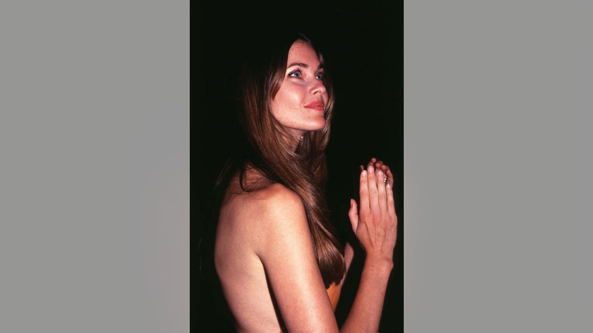Carol Alt posing to the side with her hands in a prayer pose.