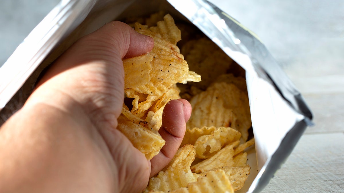 A presumption of a manus pulling retired a fistful of ridged murphy chips from a merchandise bag.