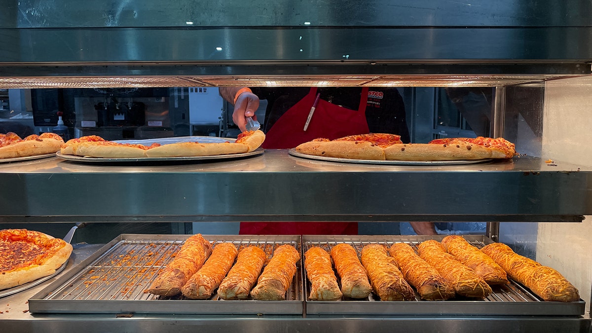 A Costco food court employee reaches for a slice of pepperoni pizza.