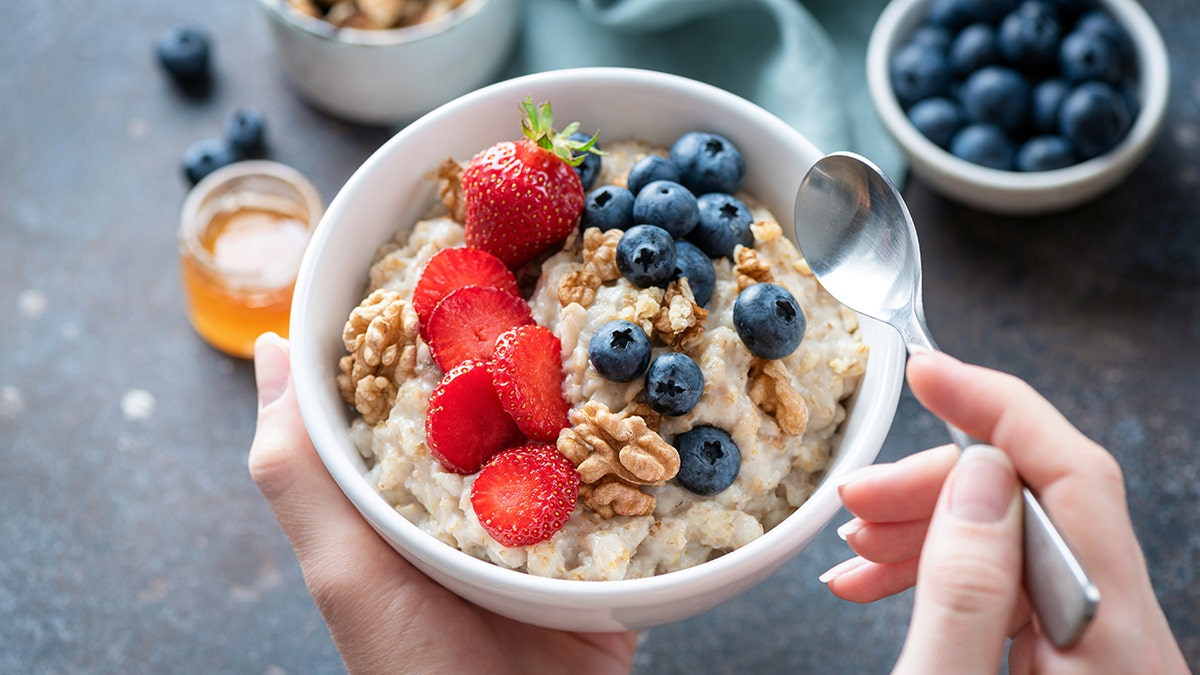 Oatmeal porridge bowl with berry fruits in female hands, closeup view.