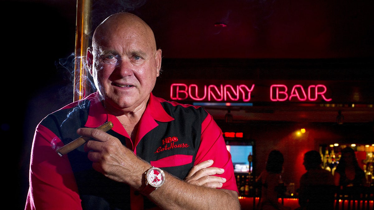 Dennis Hoff in a black and red shirt holding a cigar.