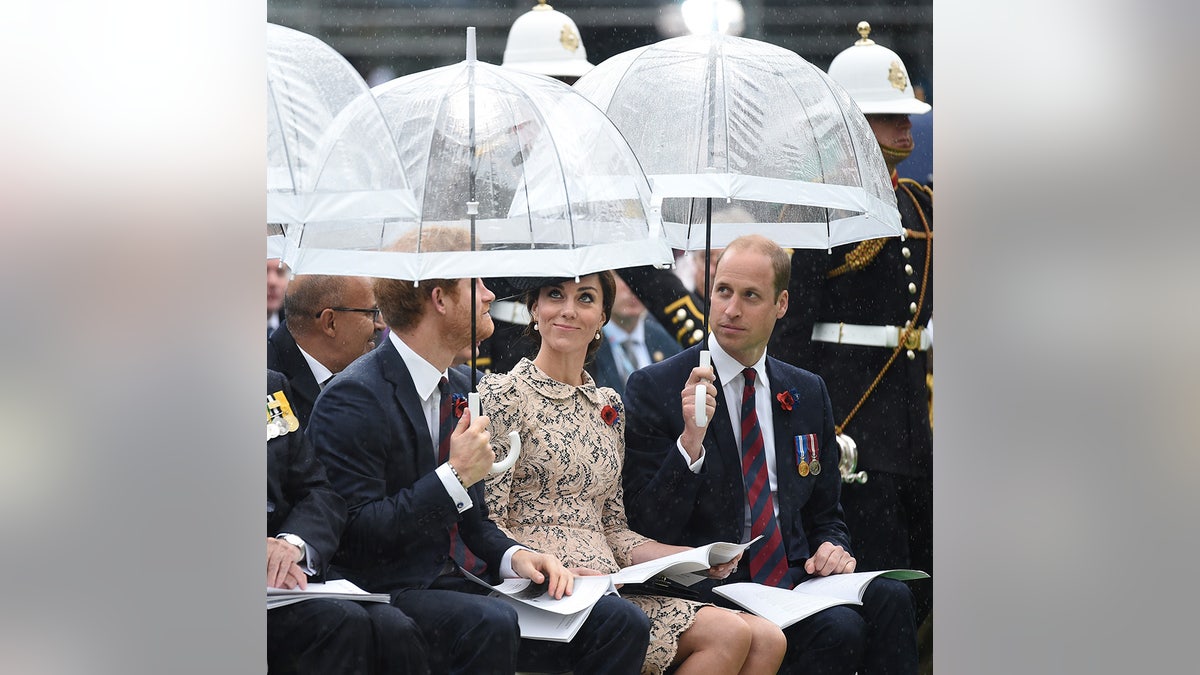 Prince Harry, Kate Middleton and Prince William sitting together in the rain with umbrellas