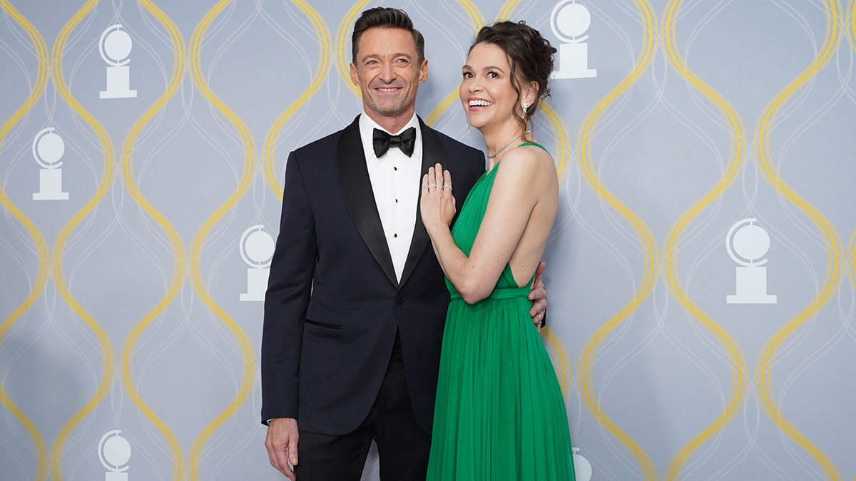 Sutton Foster wearing a green dress with her hand on Hugh Jackman's chest.