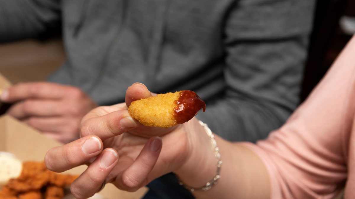 Hand dipping fried chicken in sauce