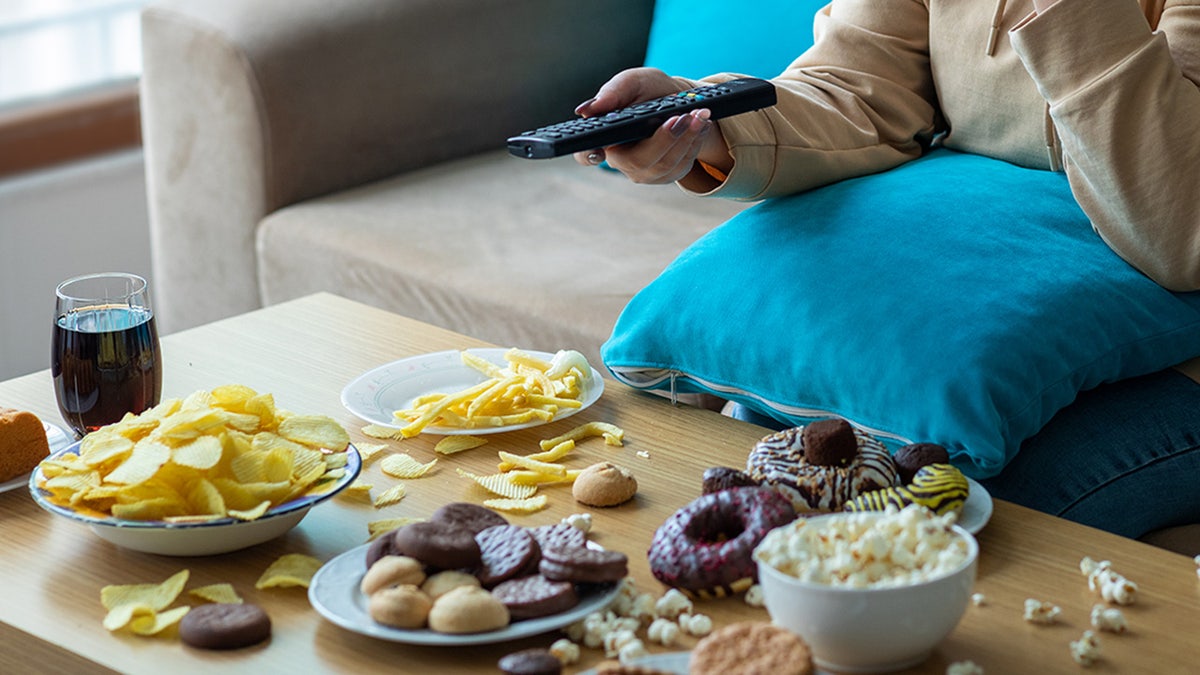 Woman sitting on sofa surrounded by junk food