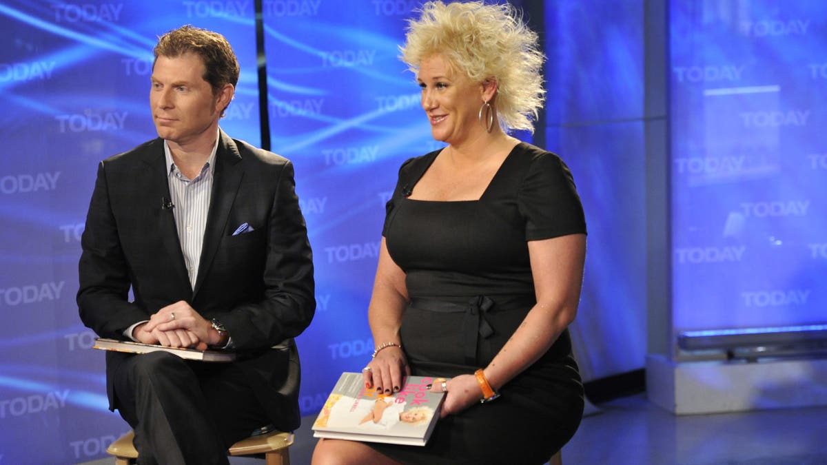 Bobby Flay wears a black suit and Anne Burrell wears a black dress during a TV event