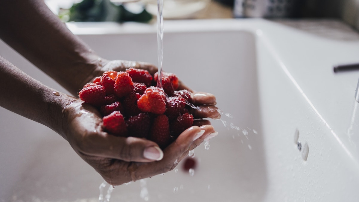 Person holding raspberries under tap water