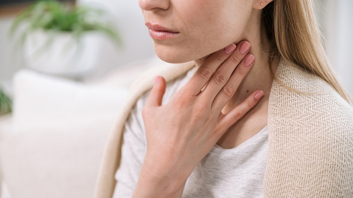Woman places hand on throat.