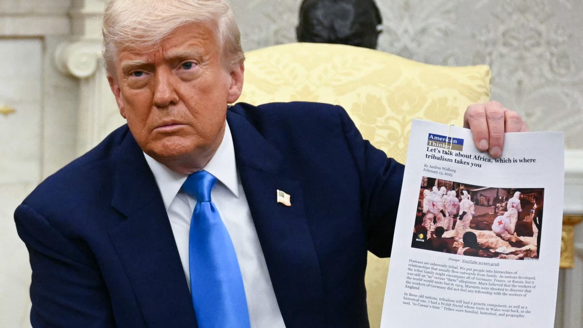 President Donald Trump holding newspaper clipping in Oval Office