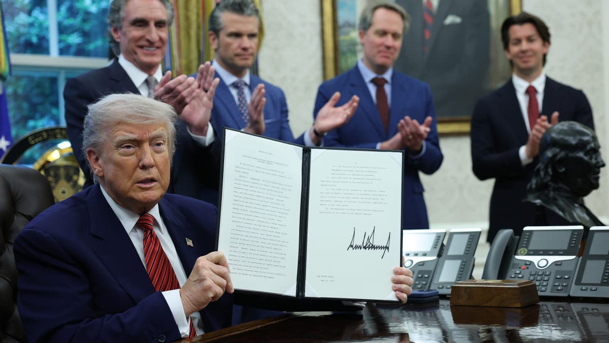 President Trump, seated, shows off signed document