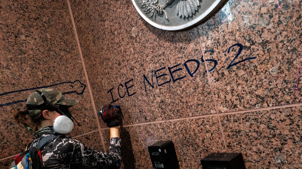 A person applies graffiti on the J.J. Pickle Federal Building during an "ICE Out of Austin" demonstration on June 09, 2025 in Austin, Texas.