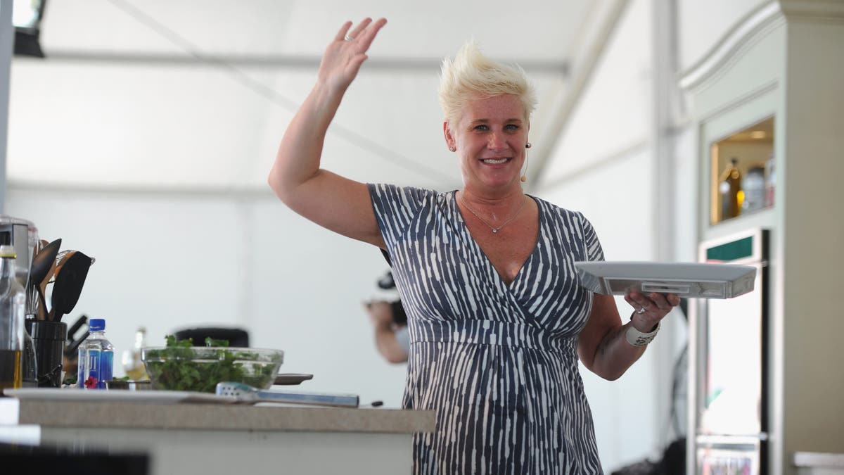 anne burrell raising her hand and holding a plate in a kitchen 