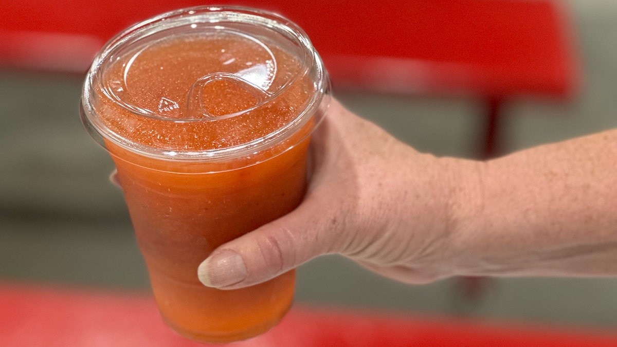 A woman's hand holds a frozen strawberry lemonade in the Costco food court area.