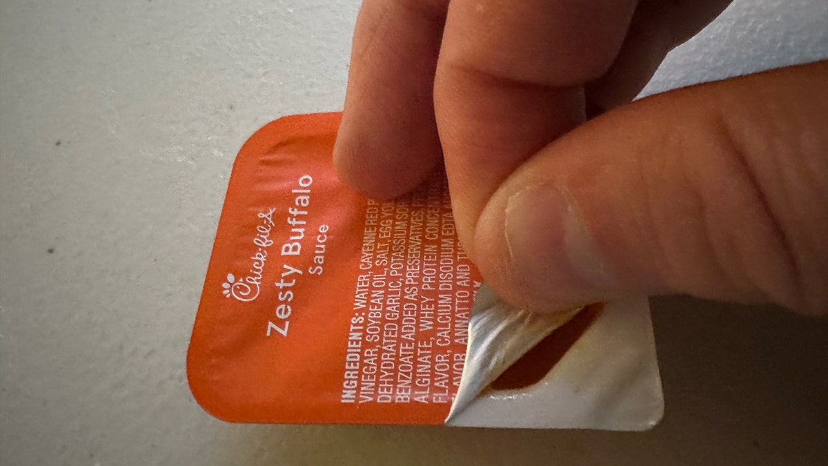 A man's hand opens a Zesty Buffalo sauce pouch from Chick-fil-A.