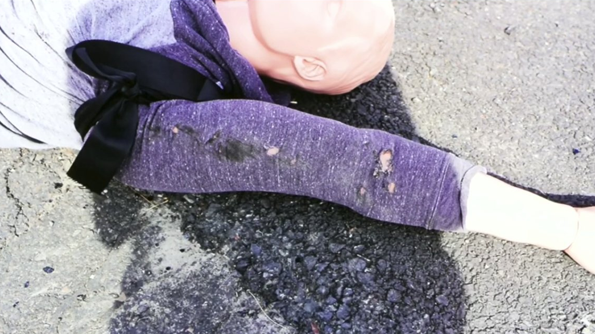a crash dummy on the ground with holes in the sleeve of its shirt