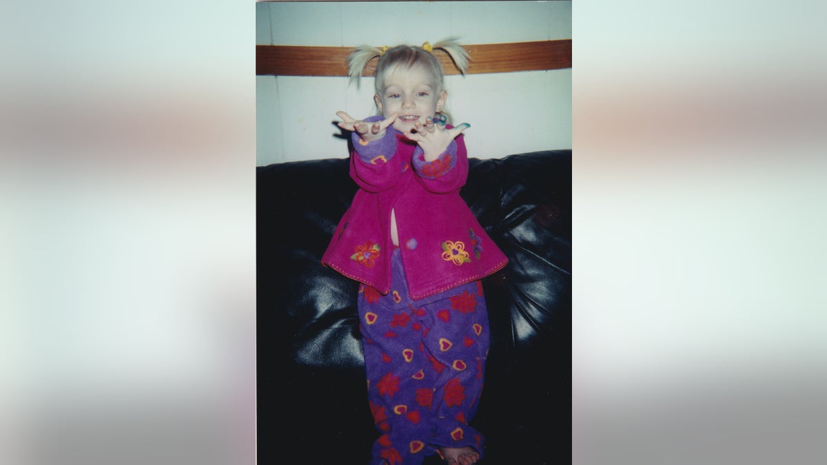 A young Emily Ferlazzo wearing a purple floral coat and pants.