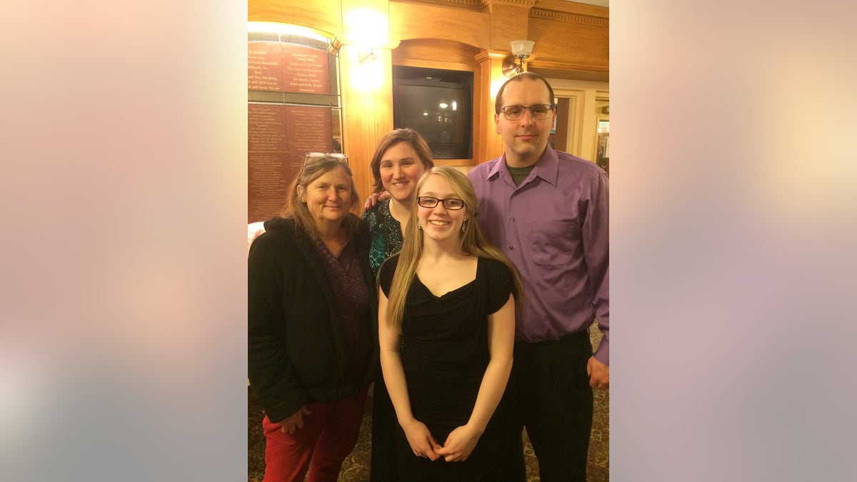 Emily Ferlazzo wears black clothes and smiles with his family.