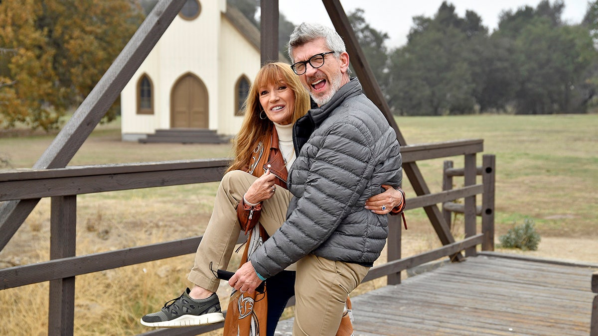 Jane Seymour holding onto Joe Lando's leg as they play around.