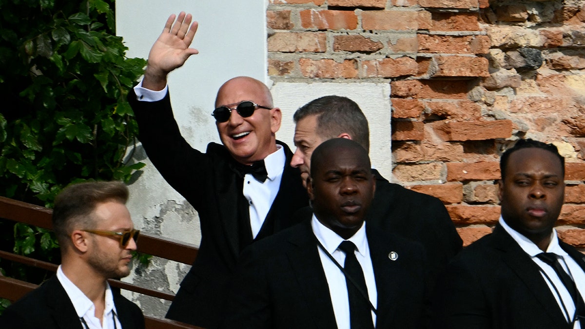 Jeff Bezos waving to the crowd in a black tuxedo