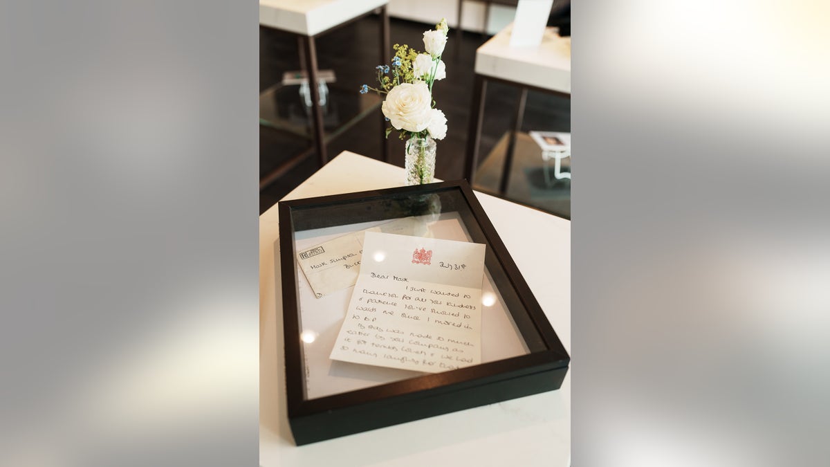 A letter written by Princess Diana is framed next to white flowers in a crystal vase.