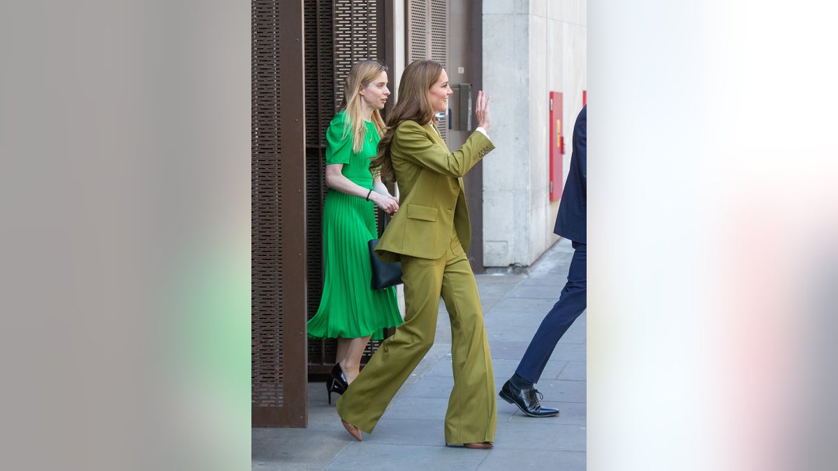 Kate Middleton waving and wearing an olive green suit.