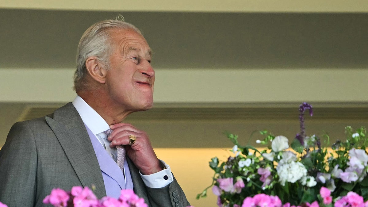 King Charles adjusting his necktie successful beforehand of flowers.