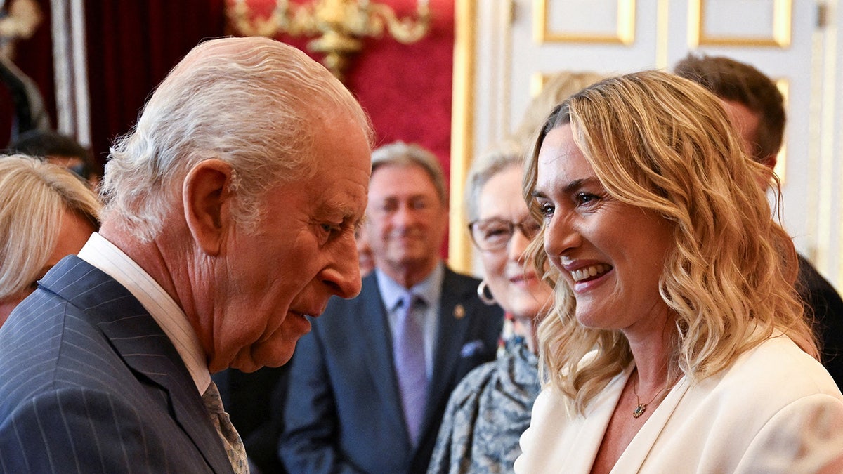 A close-up of Kate Winslet chatting with King Charles III and smiling.