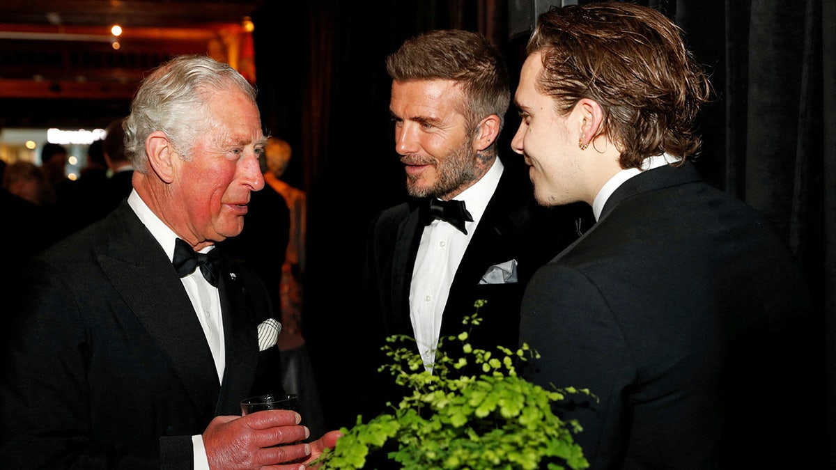 David Beckham and his son Brooklyn Beckham in a suit and bow tie chatting with King Charles.