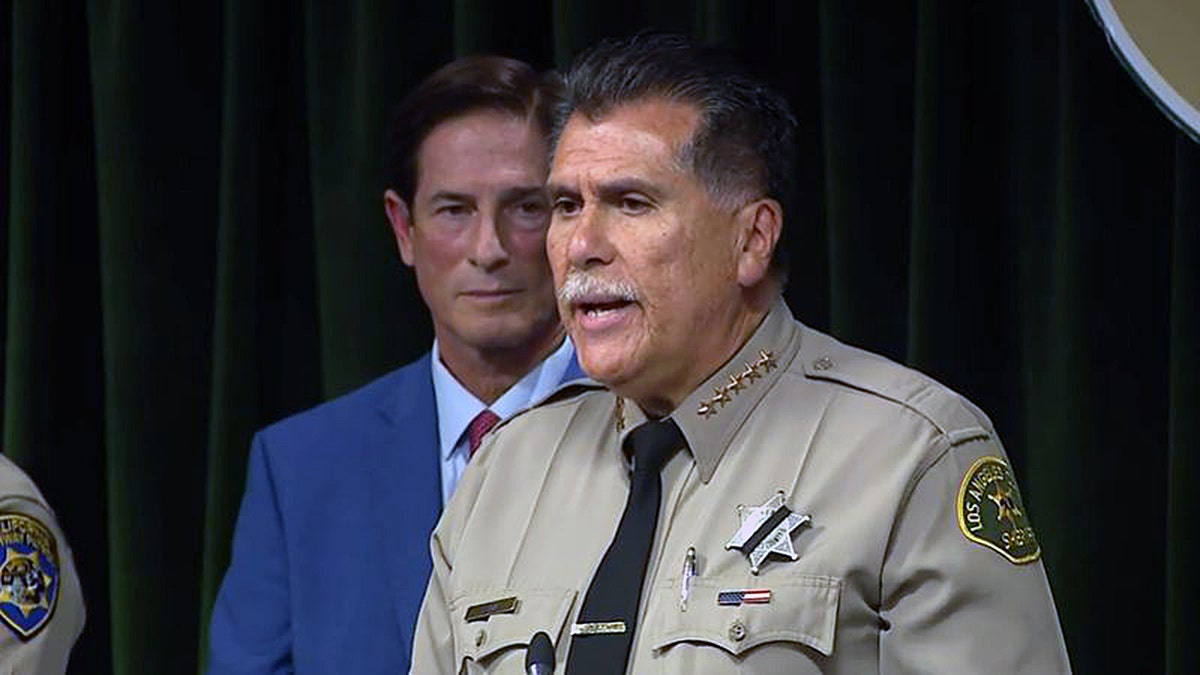 Sheriff Robert Luna speaks at a podium while DA Nathan Hochman stands behind him