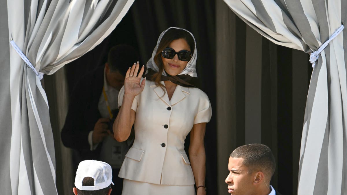 Lauren Sanchez in a white jacket and skirt waving to the camera