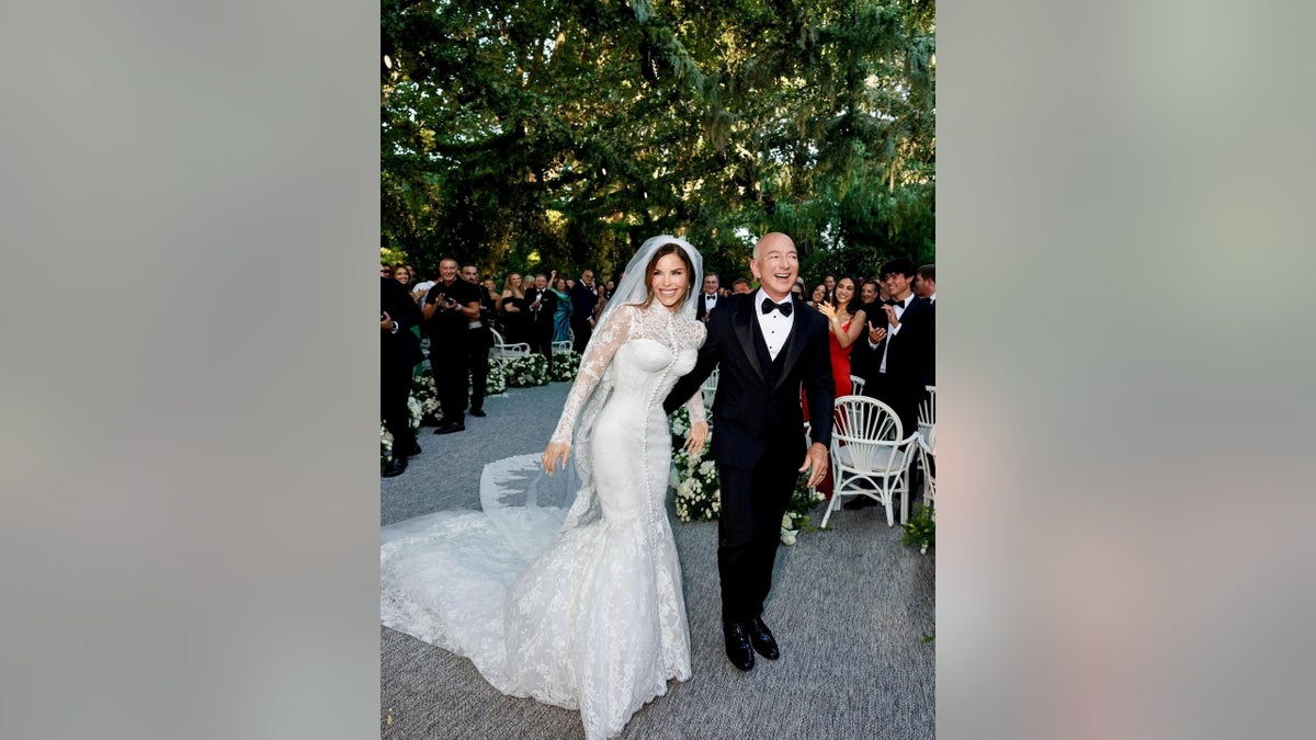 Lauren Sanchez in white mermaid wedding gown with lace sleeves and a veil beside Jeff Bezos in a classic black tuxedo