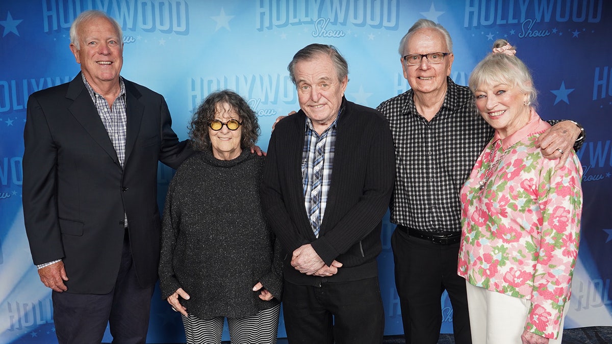 The cast of Leave It to Beaver posing together and smiling against a blue backdrop.