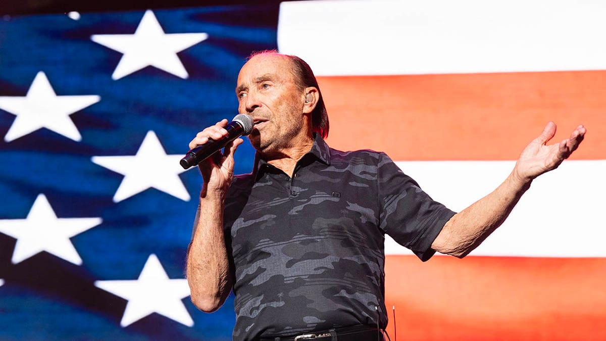 Lee Greenwood performing in front of an american flag
