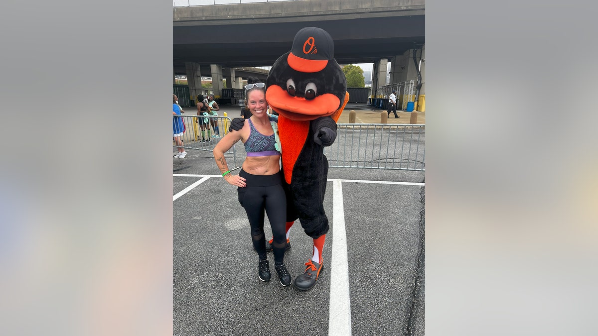 Lindsay Gutierrez in fitness wear being hugged by a mascot.