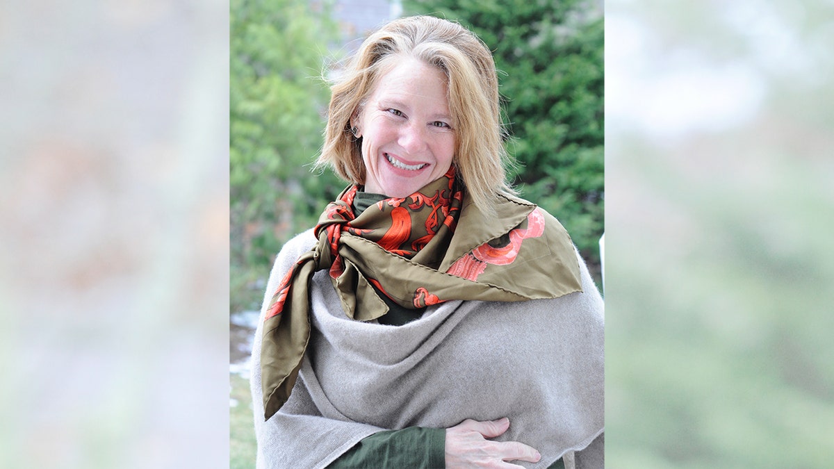 Lisa Brown Langley smiles while wearing a scarf and opinionated successful a wooded area.