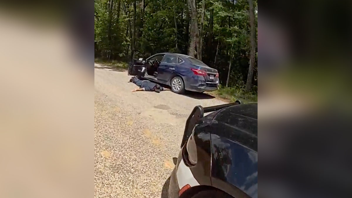 man laying on road face down next to dark colored car